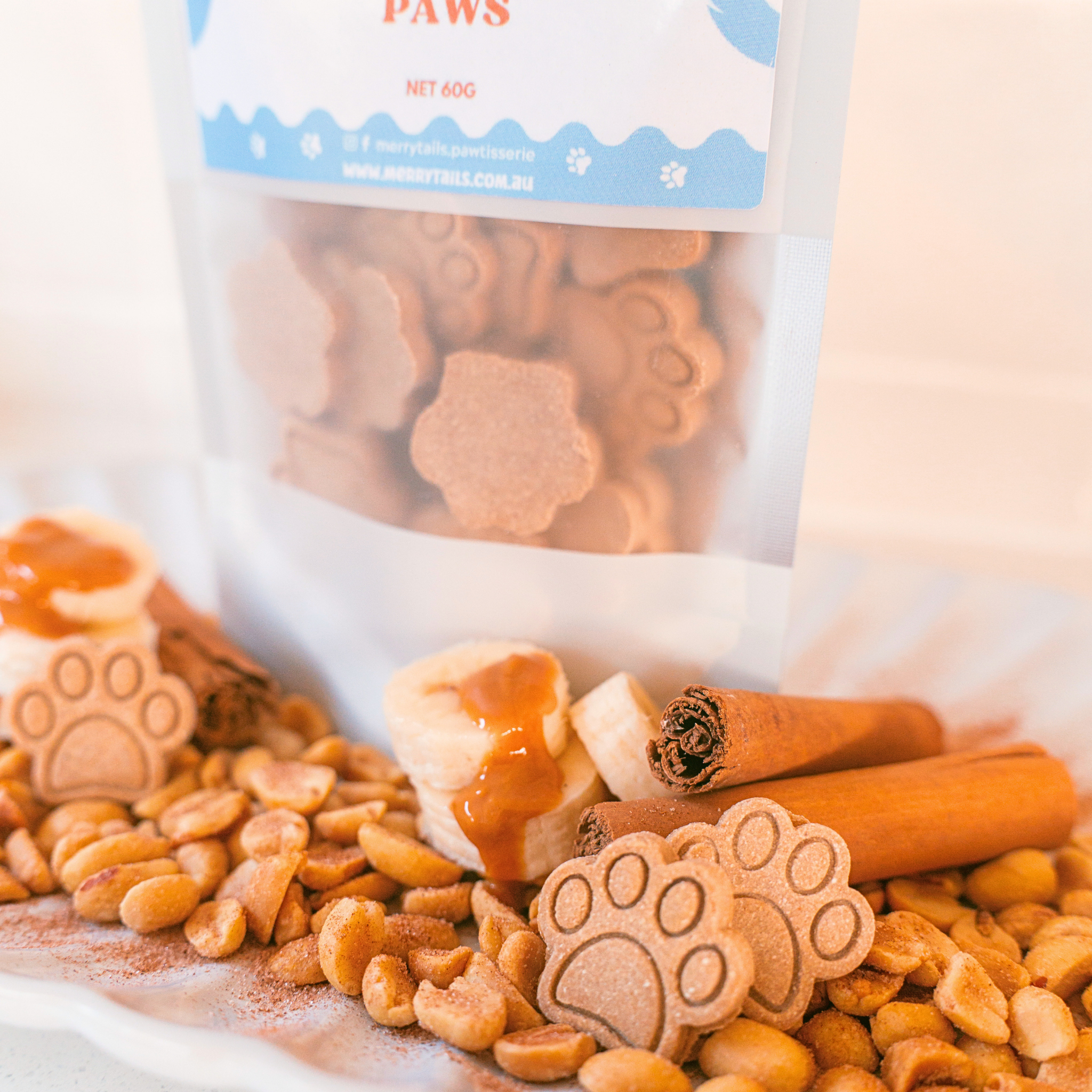 Merry Tails Pawtisserie's All Natural dog treats styled with peanut butter, banana, cinnamon and packaging in background