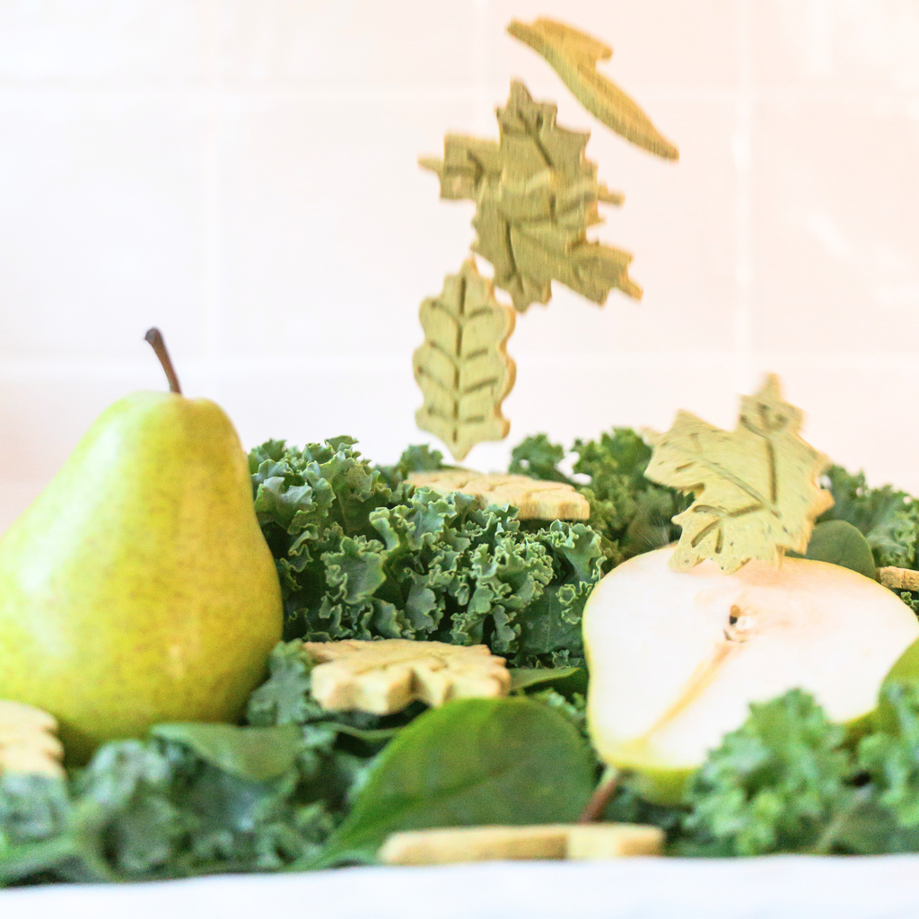 Leaf-shaped dog biscuits falling over fresh pear and greens